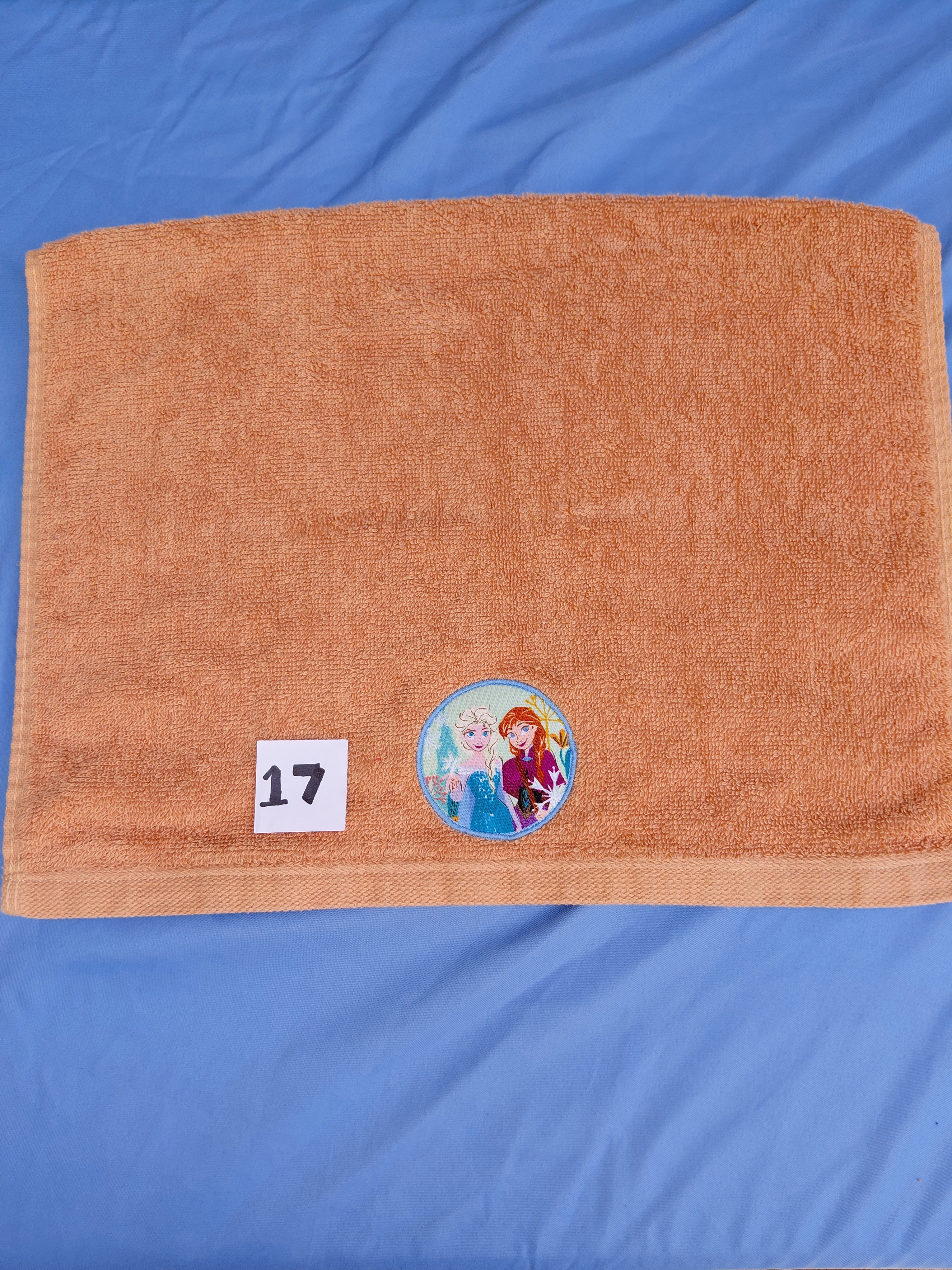 Burnt orange embellished hand towel with two princesses in one emblem, reinforced hem