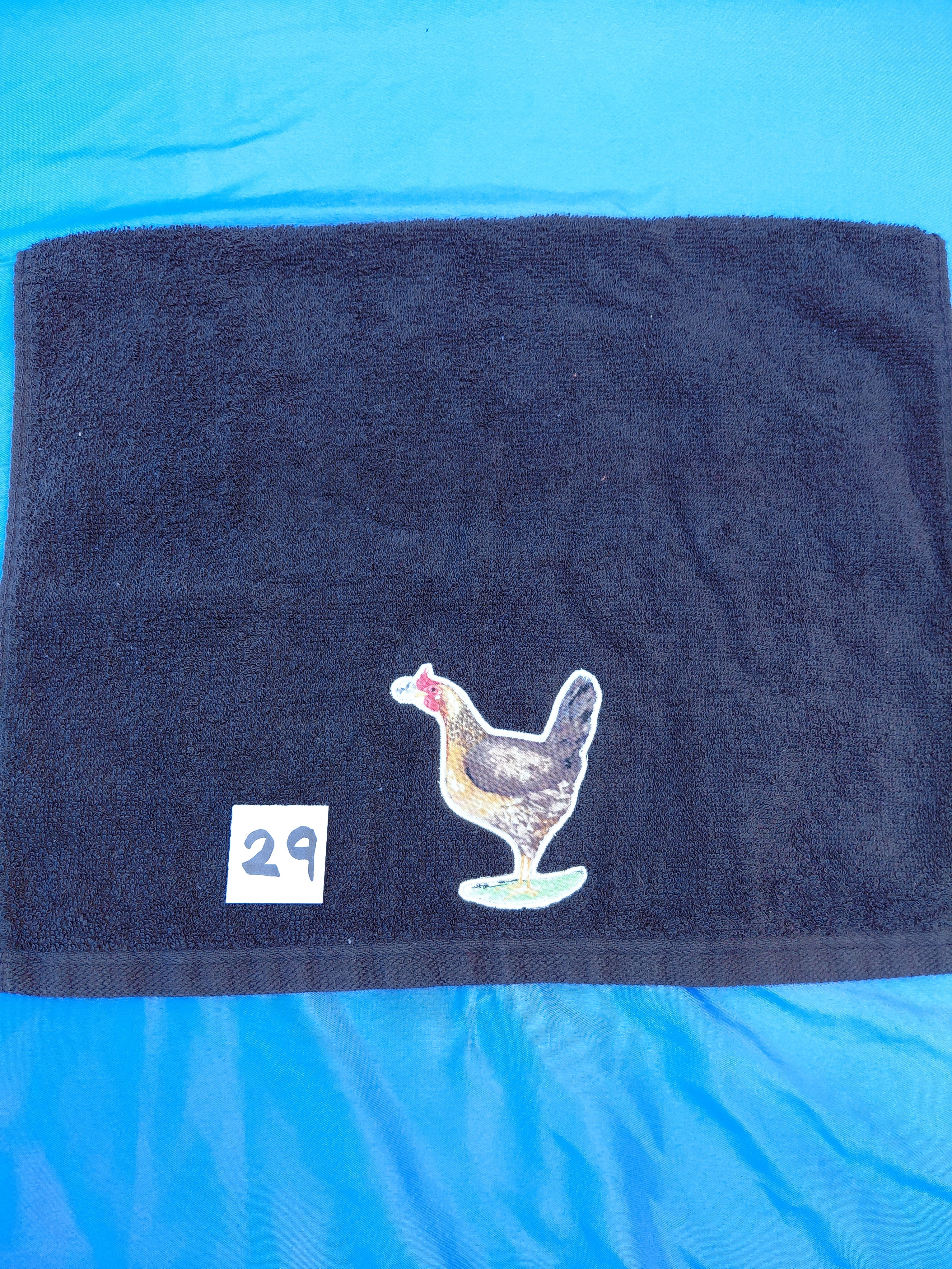 Black embellished hand towel with chicken holding a flower in its beak, reinforced hem