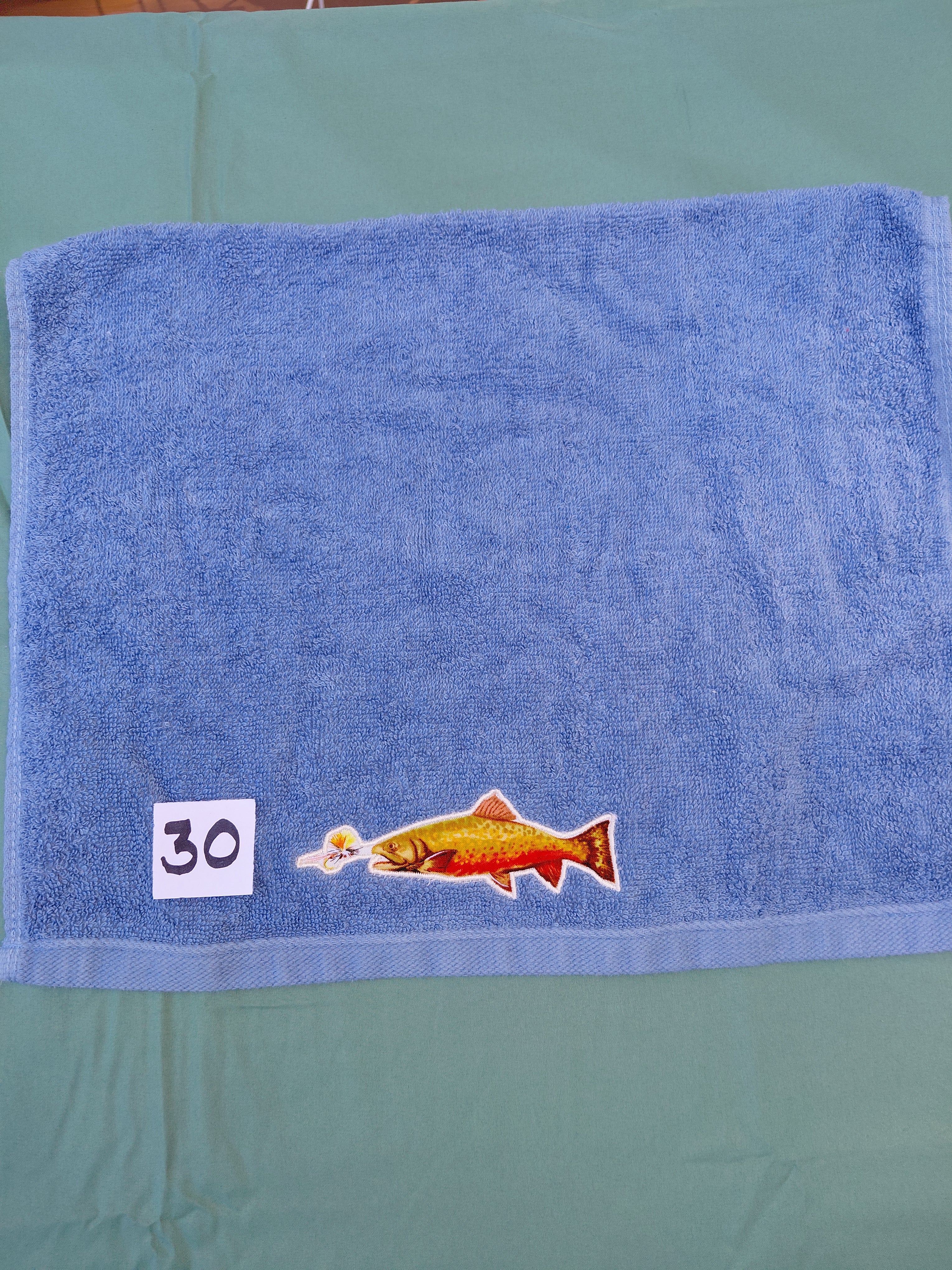 Sky blue embellished hand towel with trout about to bite a lure, reinforced hem