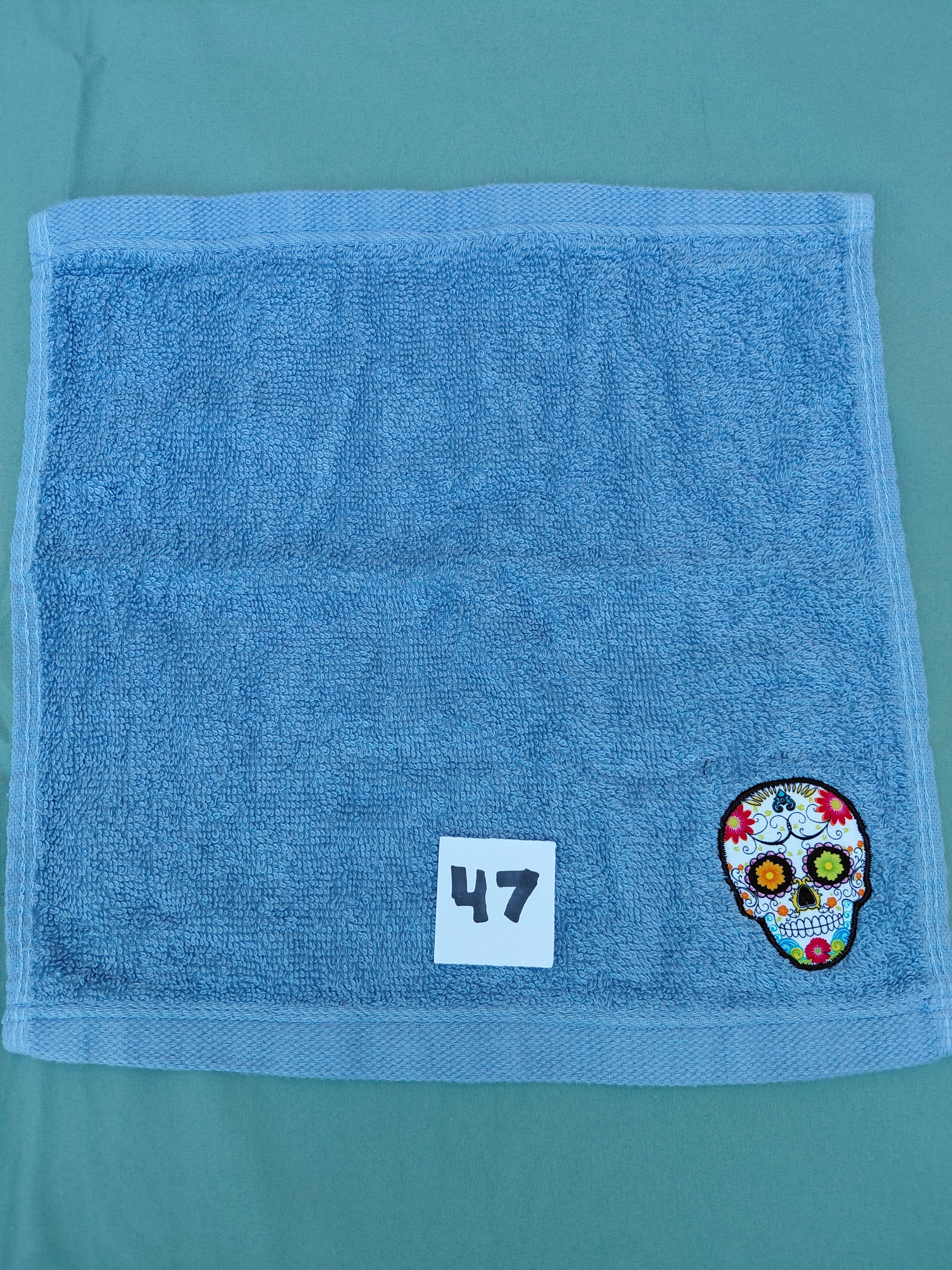 Sky blue handcrafted embellished washcloth with Day of the Dead skull appliqué, reinforced hem