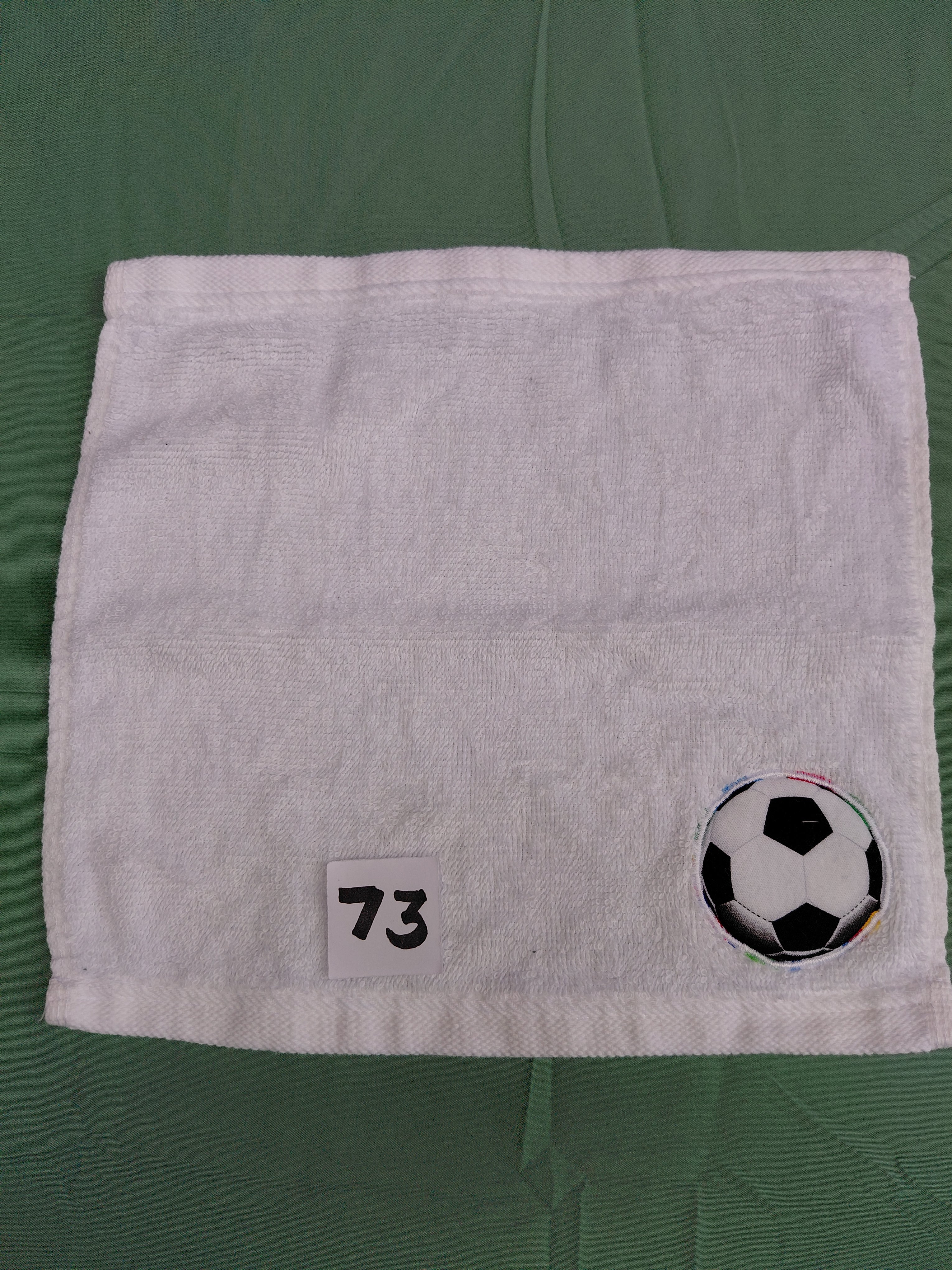 Snow white handcrafted embellished washcloth with soccer ball appliqué, reinforced hem